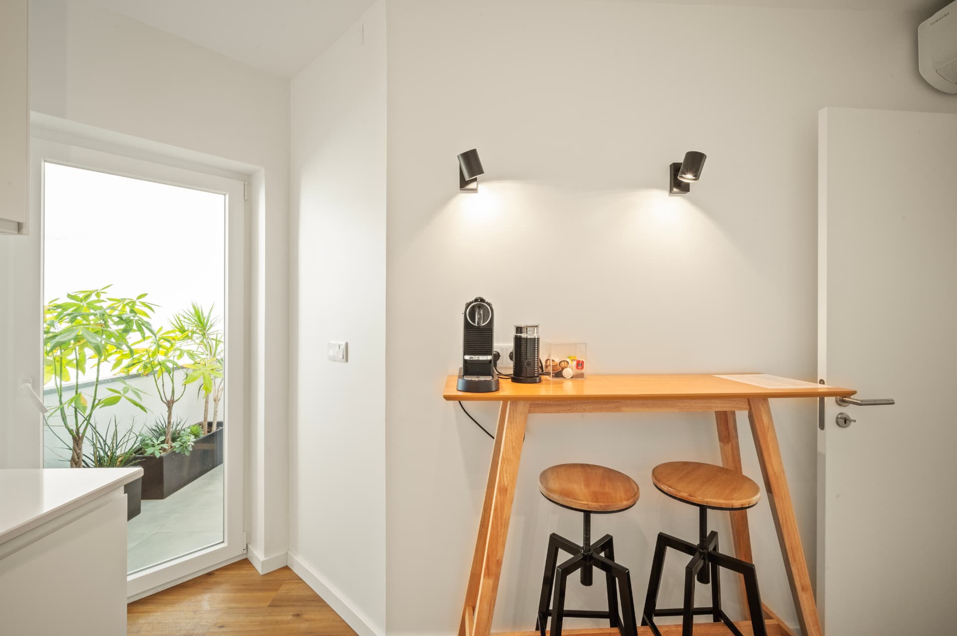 The breakfast bar by the kitchen, coffee machine ready, with the terrace door open to the plants outside