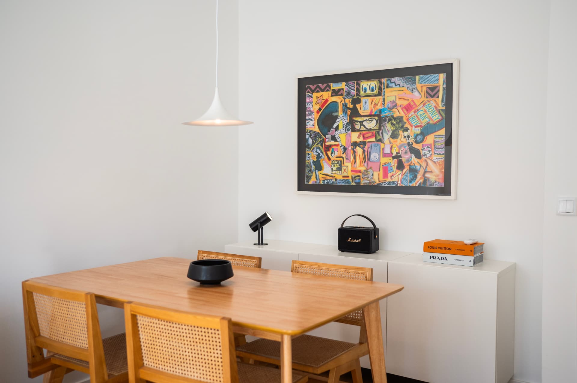 Dining table in oak with cane chairs, the pendant lamp above and framed artwork over the sideboard