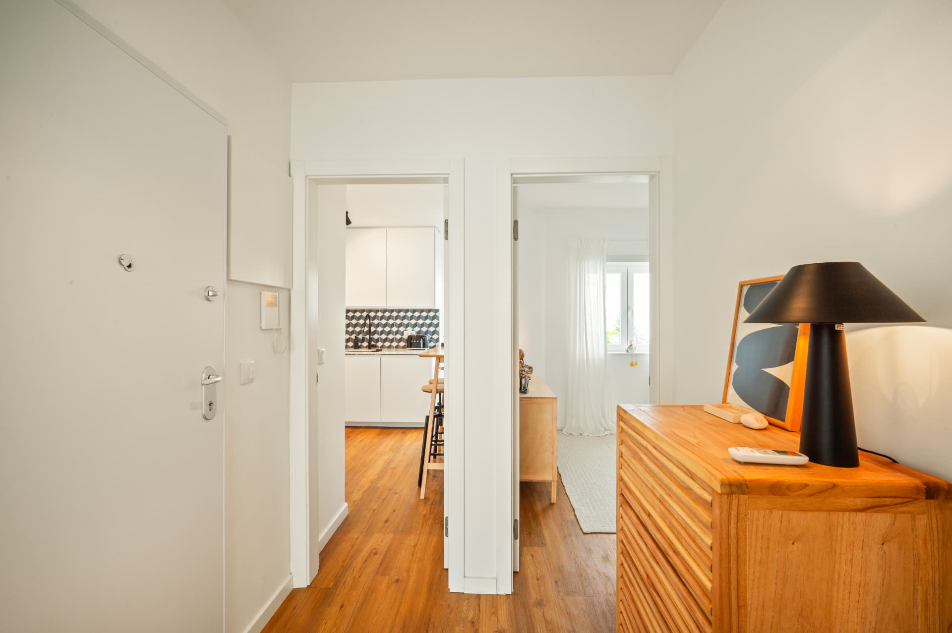 Entry hall with a pine dresser and lamp, the kitchen and a bedroom seen through open doorways