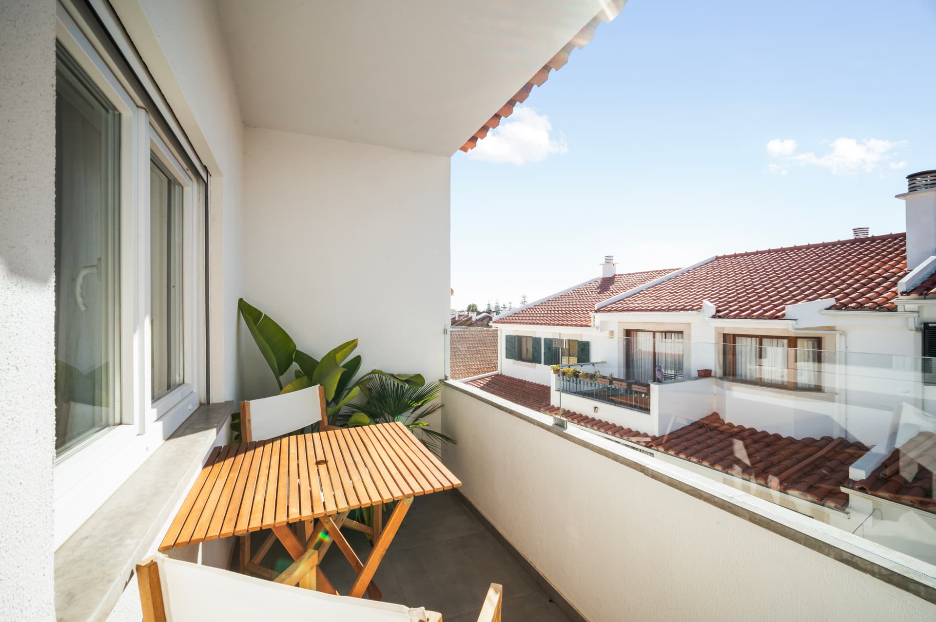 The front terrace: a wooden folding table and chairs under a covered roof, with potted plants and the terracotta rooftops of Cascais beyond the railing